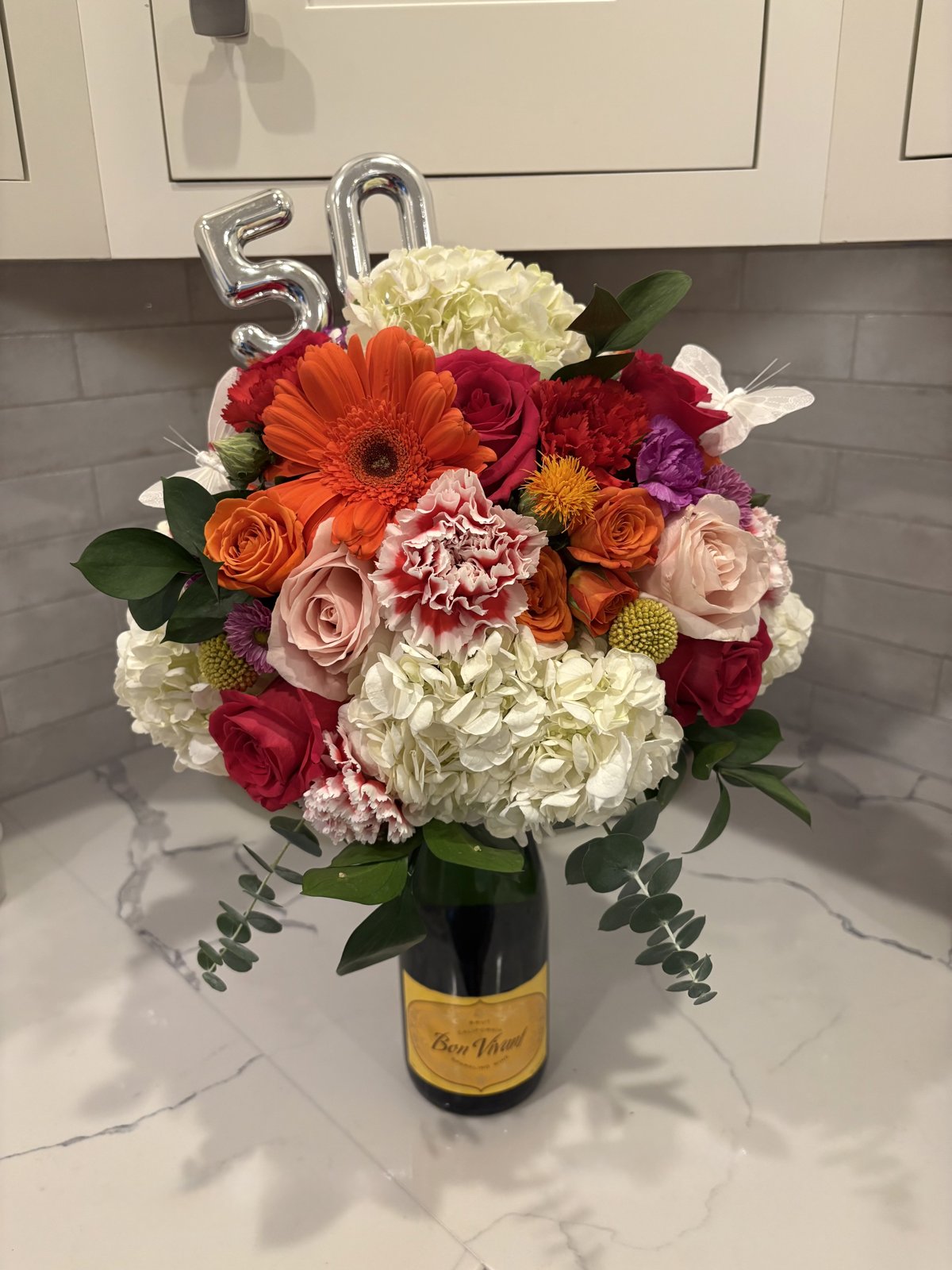 Bouquet of roses, gerbera daisies and hydrangea arranged on a bottle of sparkling wine